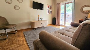 Ein Wohnzimmer mit einer Couch, einem Sessel, einem Fernseher und einem kleinen Tisch mit einer Kerze.