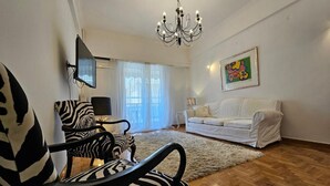 Un salon avec un fauteuil à motifs zébrés, un canapé blanc, un lustre et un tableau accroché au mur.