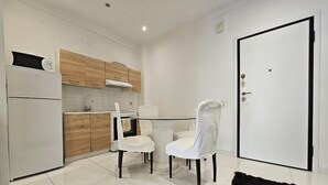 Une cuisine compacte avec des appareils électroménagers blancs, des meubles en bois et un coin repas équipé de deux chaises.