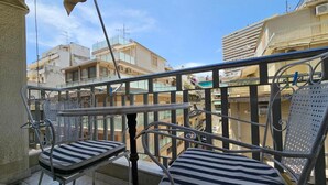Un balcon avec deux chaises à rayures et une table, donnant sur un quartier résidentiel avec des immeubles.