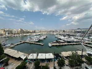 A marina with boats docked, a cityscape in the background, and outdoor seating areas. - Serenity View Apartment - Marina Zeas (Pireas)