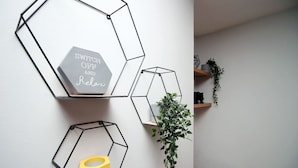 Paredes com prateleiras geométricas exibindo uma placa, uma planta e um objeto amarelo.