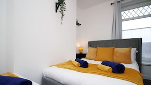 Quarto de hotel com cama, mesa de cabeceira, luminária e janela com cortinas.