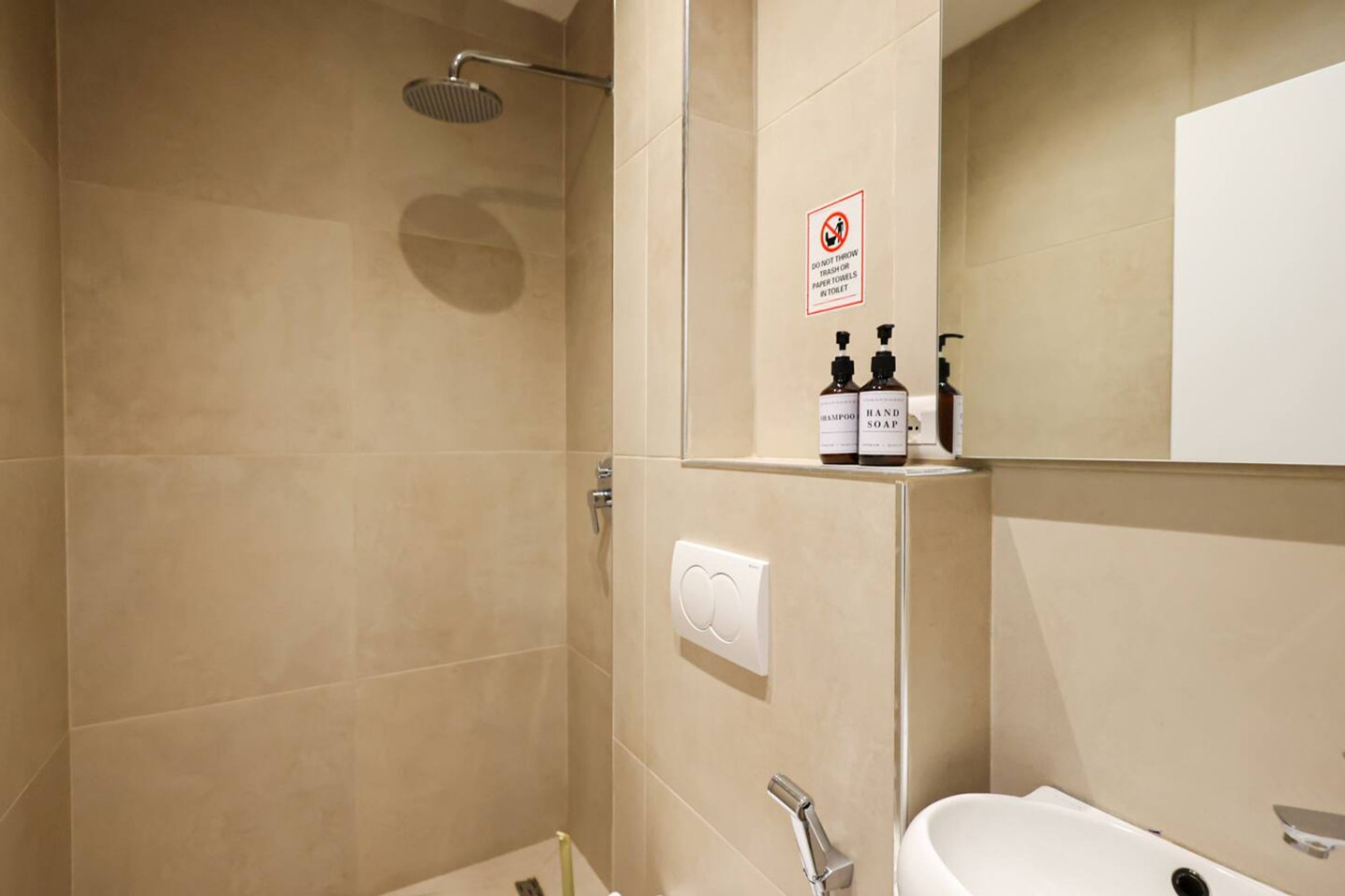 A bathroom with a shower, a toilet, and a sink. There is a sign prohibiting the disposal of trash in the toilet.