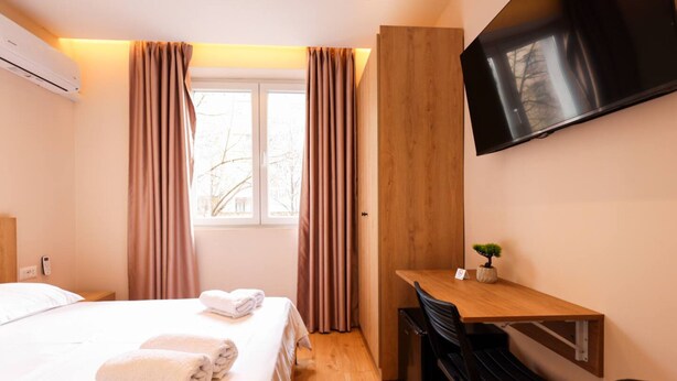 A hotel room with a bed, a desk, a chair, a television, and a window with curtains. - Grandstay Tirana Central 01 (Tiranë)