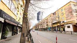 A street with buildings, a tree, and a closed shop with a sign that reads 'Tattoo'. - Grandstay Tirana Central 01 (Tiranë)