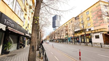 A street with buildings, a tree, and a closed shop with a sign that reads 'Tattoo'.