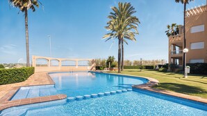 Una piscina con acqua cristallina, circondata da palme e un edificio con balconi.