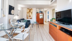 Un soggiorno moderno con un tavolo da pranzo in vetro, sedie bianche, un divano, una TV e un mobile in legno.