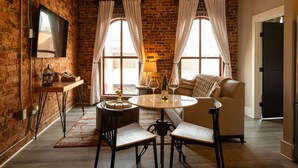 A cozy room with a brick wall, a round table with chairs, a sofa, and a TV mounted on the wall. - Three Trails Downtown Elkin Yadkin Valley (Elkin)