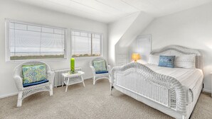Une chambre aux murs blancs, avec un lit, deux fauteuils en osier, une petite table et un radiateur.