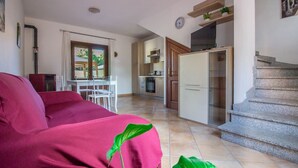 Una sala de estar con sofá, un comedor con mesa y sillas, una cocina con armarios y electrodomésticos, y una escalera.