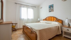 Un dormitorio con cama de madera, mesita de noche, una silla, escritorio y ventana con cortinas.