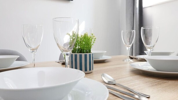 Mesa de jantar com pratos brancos, copos transparentes e caneca listrada com uma pequena planta.