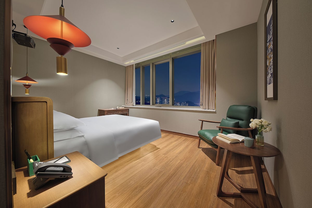 Une chambre d’hôtel équipée d’un lit, d’un bureau, d’une chaise et d’une fenêtre donnant sur la ville.