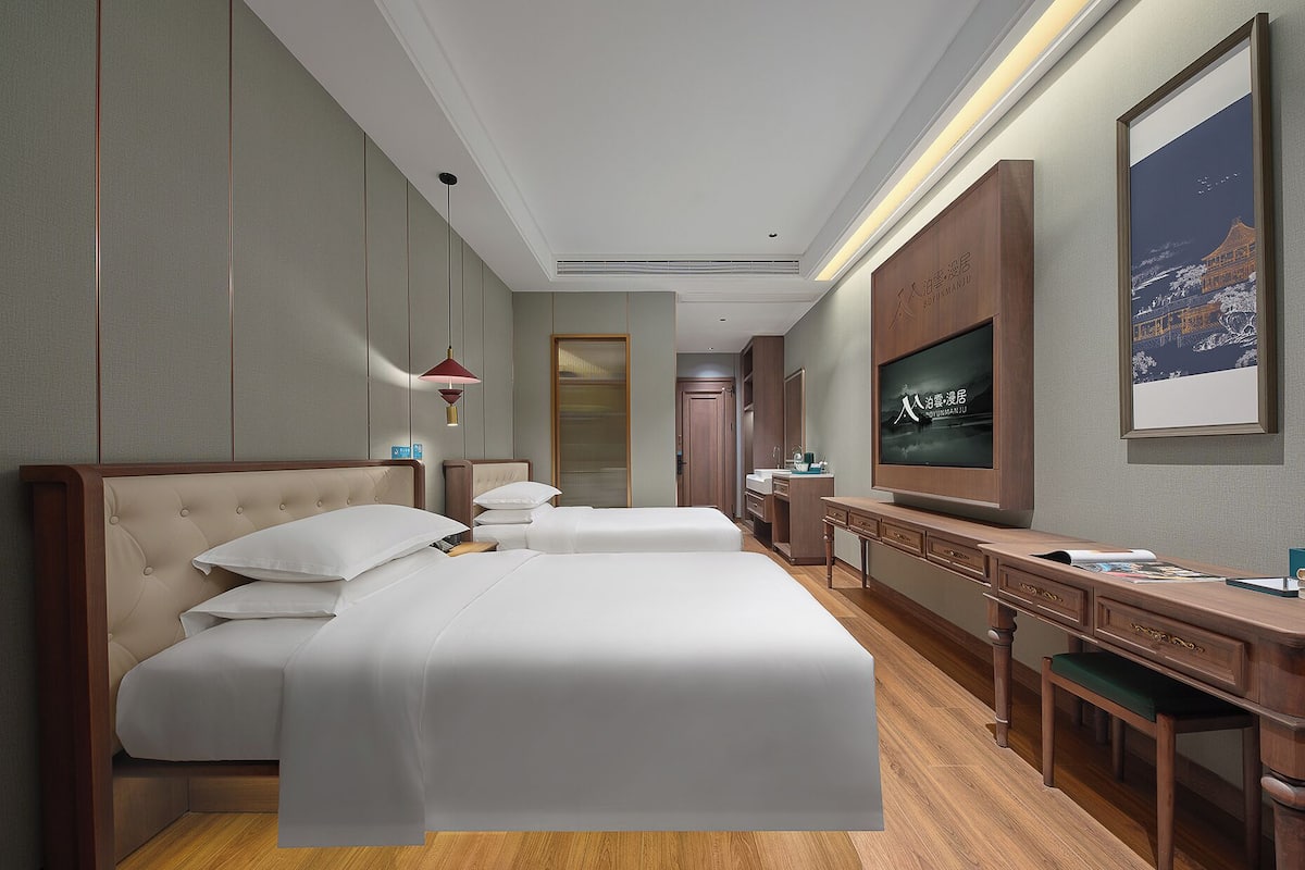 Une chambre d’hôtel avec deux lits, un bureau, une télévision et une salle de bain que l’on aperçoit à l’arrière-plan.