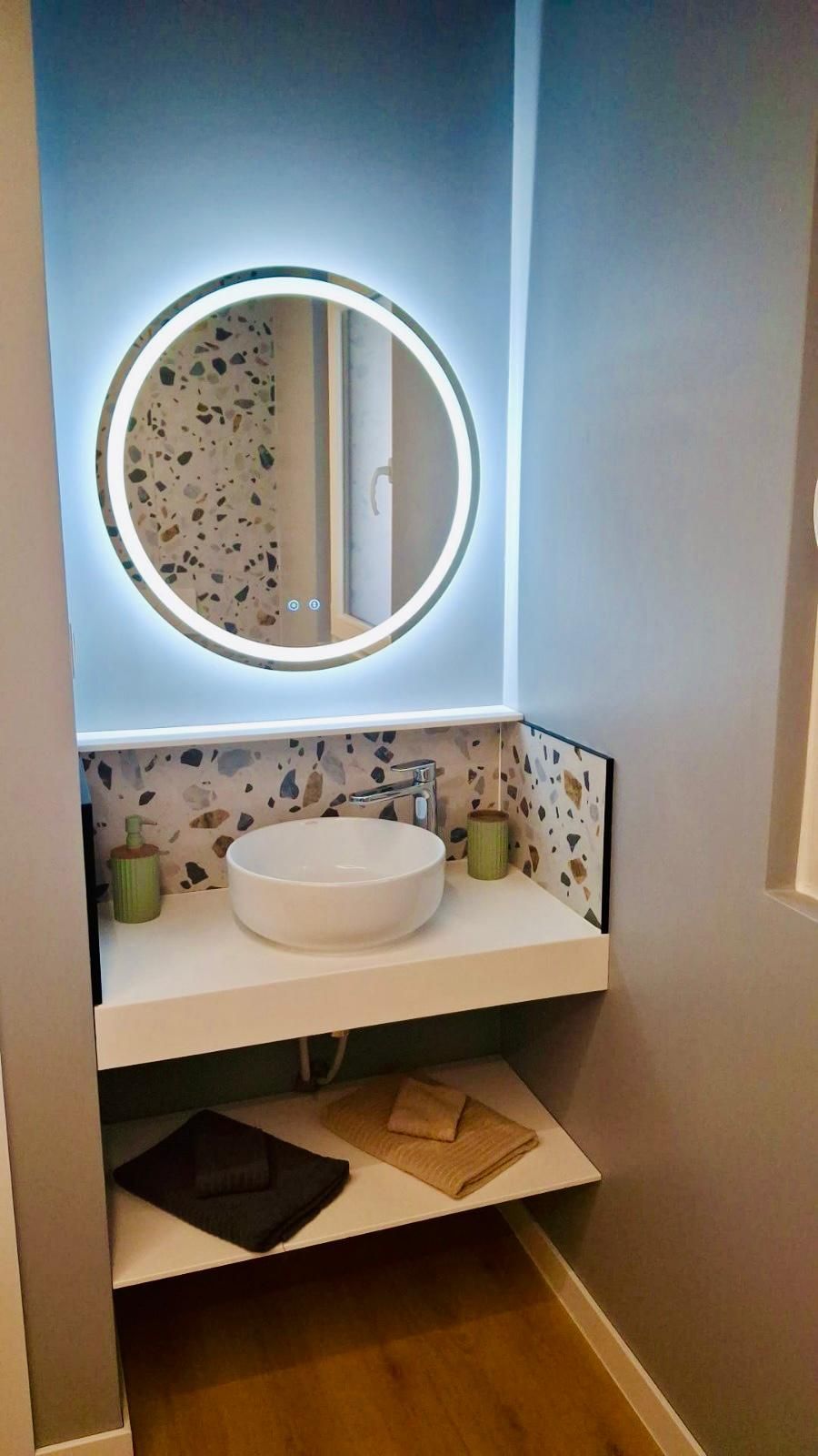 A bathroom with a round mirror, white sink, and terrazzo backsplash.