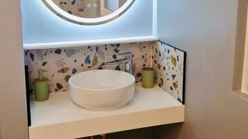 A bathroom with a round mirror, white sink, and terrazzo backsplash.