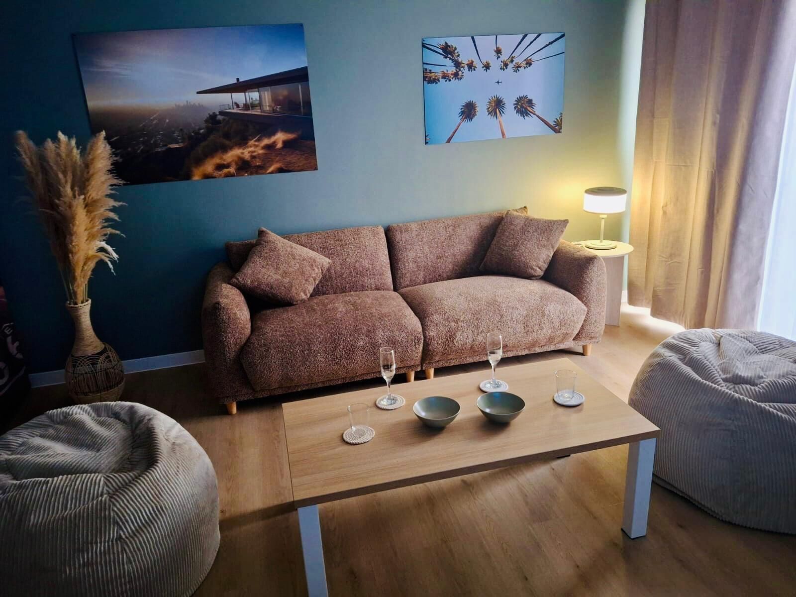 A modern living room with a sofa, a coffee table with bowls, a vase with dried plants, and two wall-mounted lamps.