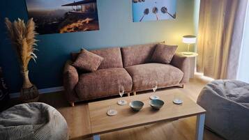 A modern living room with a sofa, a coffee table with bowls, a vase with dried plants, and two wall-mounted lamps.