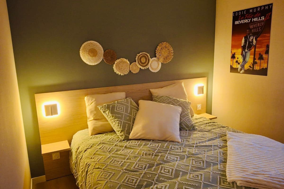A neatly made bed with patterned bedding, a wall-mounted decorative wall hanging, and a poster on the wall.