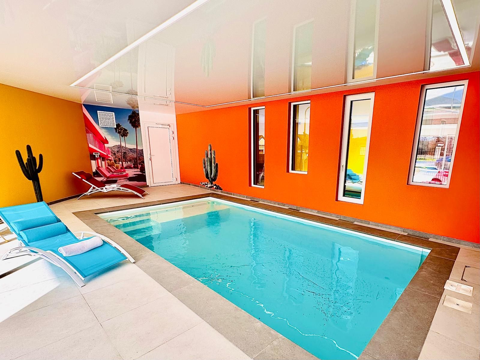An indoor swimming pool with blue lounge chairs and a mural on the wall.