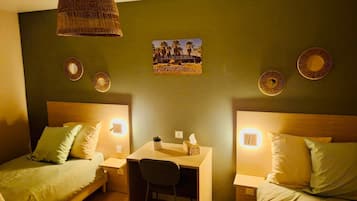 Une chambre avec deux lits, un bureau et une chaise. Il y a des lampes fixées au mur et un tableau représentant des palmiers.
