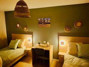 A room with two beds, a desk, and a chair. There are wall-mounted lights and a picture of palm trees. - Le California (Neuf-Mesnil)