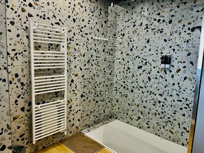 A modern bathroom with a shower area, a white towel rack, and a terrazzo floor. - Le California (Neuf-Mesnil)