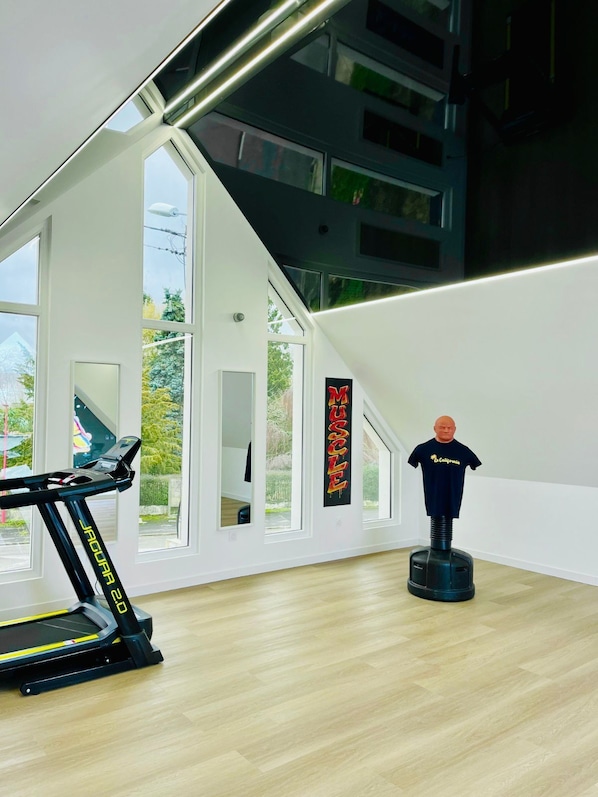 A modern room with a treadmill, a mannequin, and large windows. - Le California (Neuf-Mesnil)