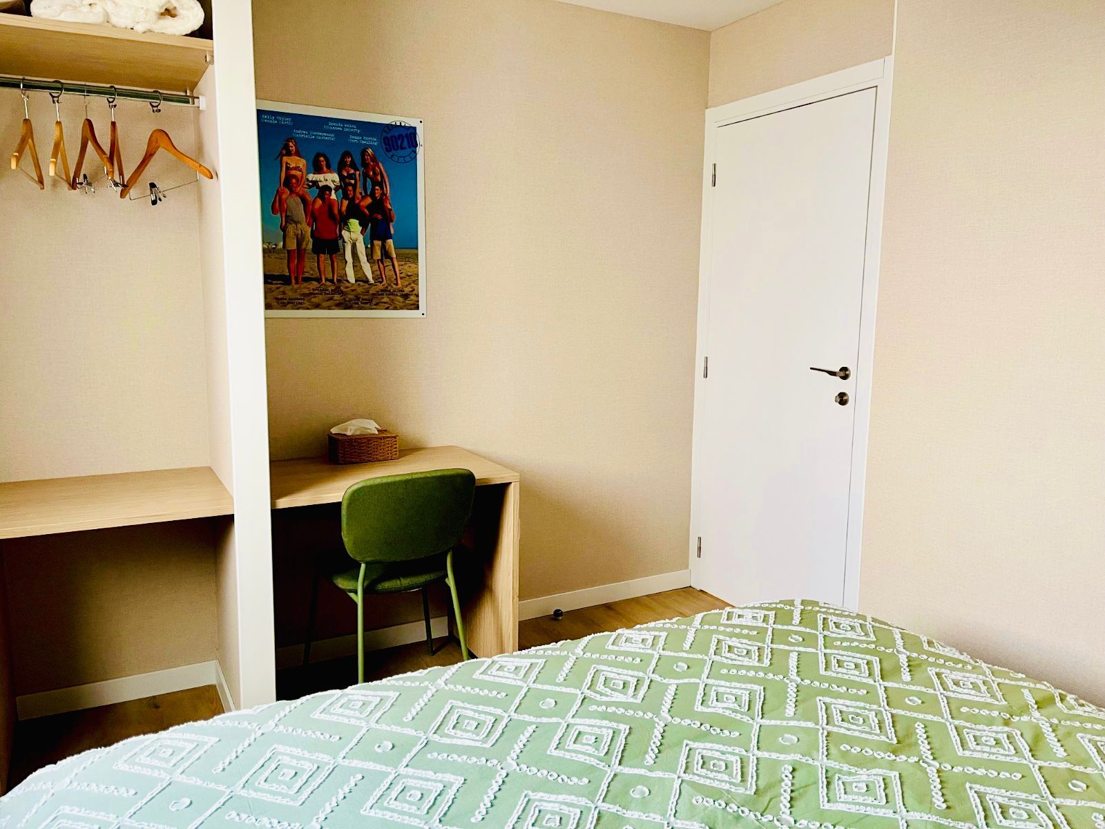 A bedroom with a bed, a desk, a chair, a wardrobe, and a poster on the wall.