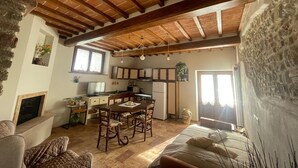 A rustic kitchen with wooden beams, a dining area with a table and chairs, and a stone wall. - Cozy apartment: Your oasis of paradise in the countryside (Anghiari)