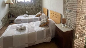A bedroom with two beds, a stone wall, a window with curtains, a lamp, and a bedside table. - Cozy apartment: Your oasis of paradise in the countryside (Anghiari)