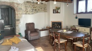 A cozy living room with a stone fireplace, wooden ceiling beams, a dining table, and a comfortable seating area. - Cozy apartment: Your oasis of paradise in the countryside (Anghiari)