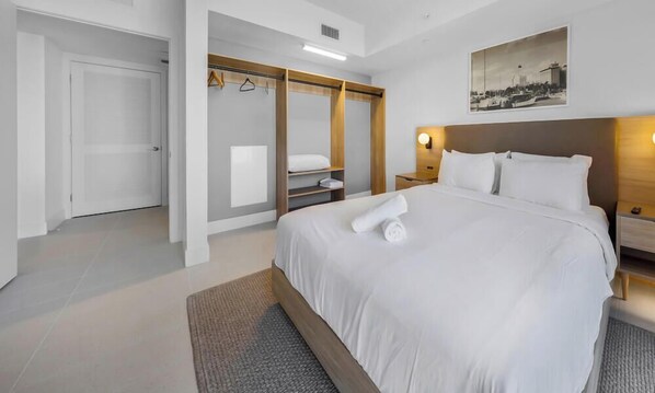 Une chambre d’hôtel avec un grand lit, un dressing, une table de chevet et une lampe fixée au mur.