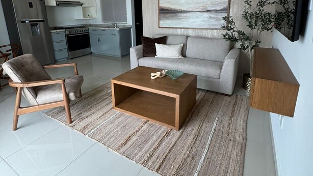 Ein modernes Wohnzimmer mit einer Couch, einem Couchtisch und einem Essbereich, im Hintergrund befindet sich eine Küche.