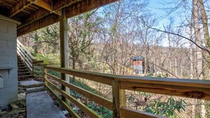 A covered outdoor area with a wooden railing, a concrete staircase, and a view of a forested area. - *Amazing 3BD w/ Hot Tub | Fire Pit + Pool Access* (Gatlinburg)