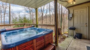A hot tub on a covered deck with a view of trees and a door to the right. - *Amazing 3BD w/ Hot Tub | Fire Pit + Pool Access* (Gatlinburg)