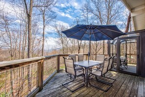 A wooden deck with a table and chairs, an umbrella, and a glass door leading to a deck area. - *Amazing 3BD w/ Hot Tub | Fire Pit + Pool Access* (Gatlinburg)