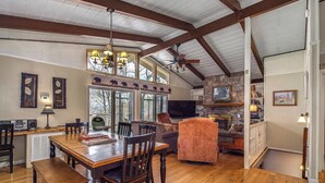 A spacious dining area with a wooden table and chairs, a stone fireplace, and a television in the background. - *Amazing 3BD w/ Hot Tub | Fire Pit + Pool Access* (Gatlinburg)