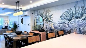 A modern dining area with a large table, chairs, and a wall mural of tropical foliage.