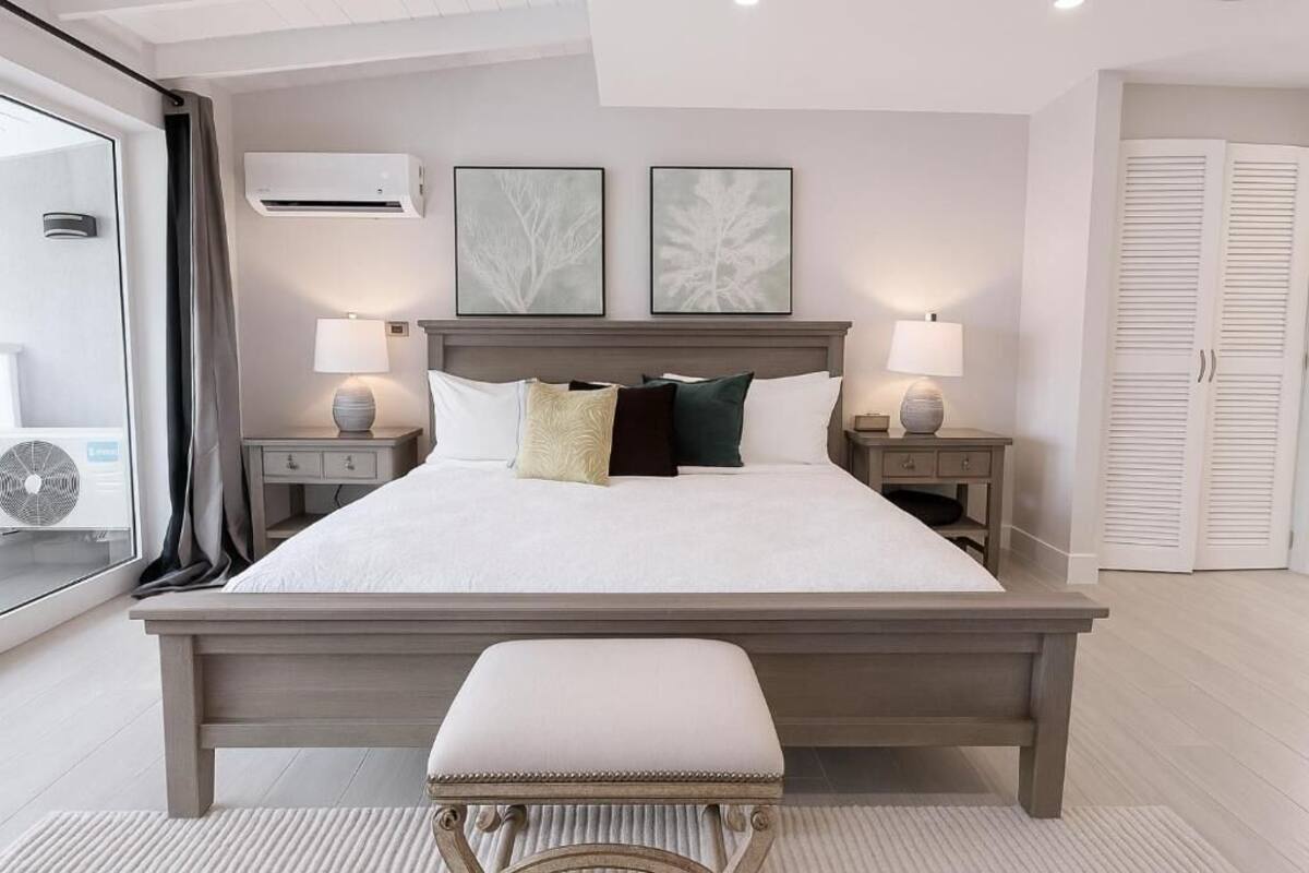 A bedroom with a large bed, bedside tables, a bench, and artwork on the wall.