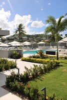 Zona de piscina con sillones de descanso, sombrillas y vistas a una zona residencial al fondo.
