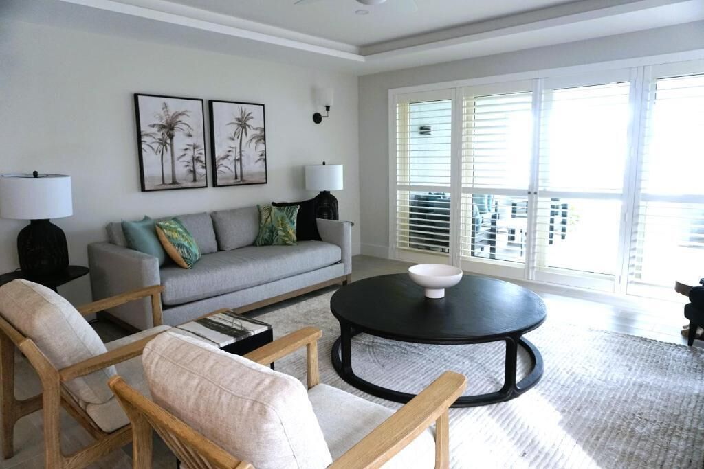 A living room with a sofa, two armchairs, a coffee table, and a large window with blinds.