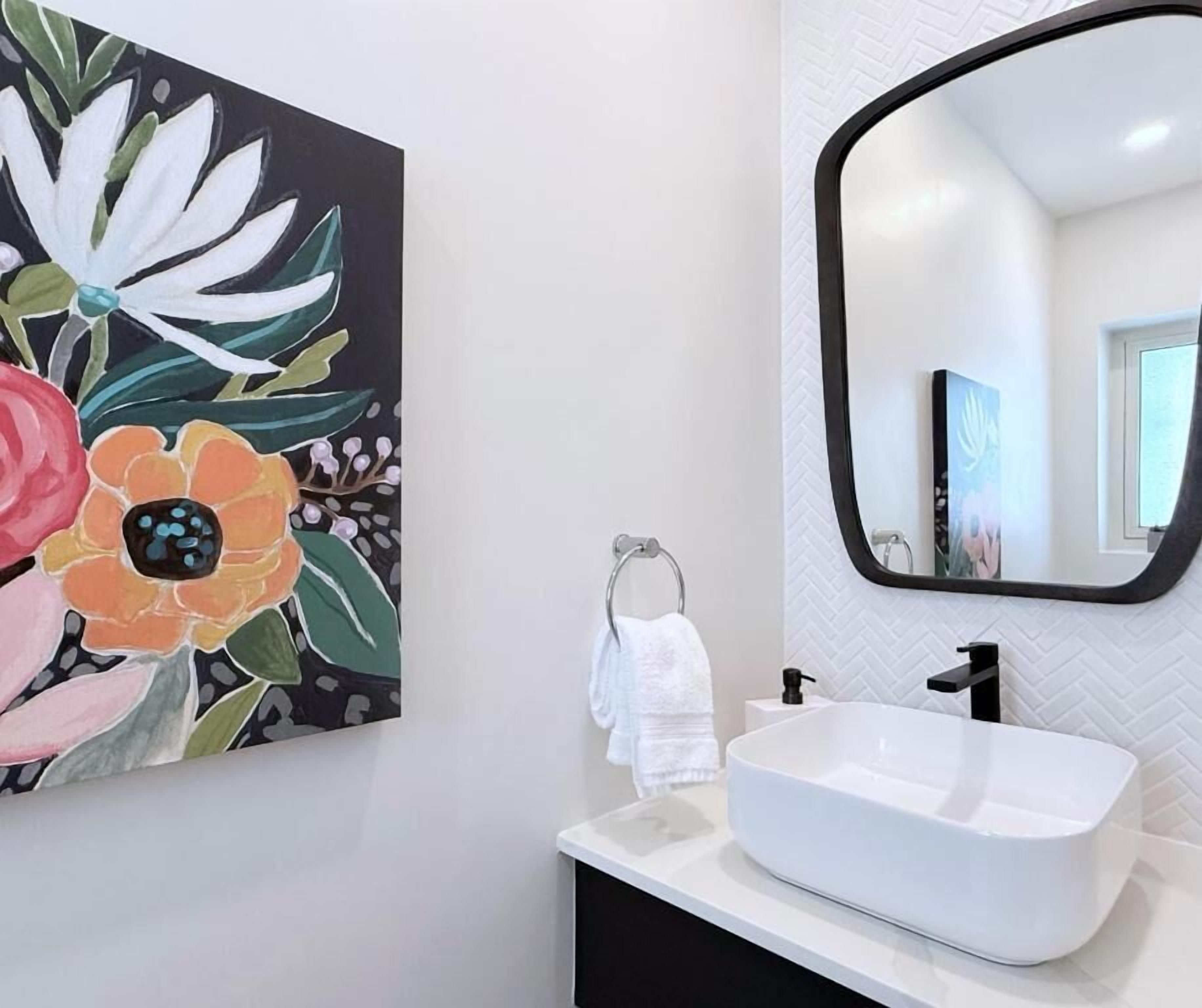 Een badkamer met een wit wastafel, een zwarte kraan, een witte handdoek en een spiegel met een zwarte lijst.