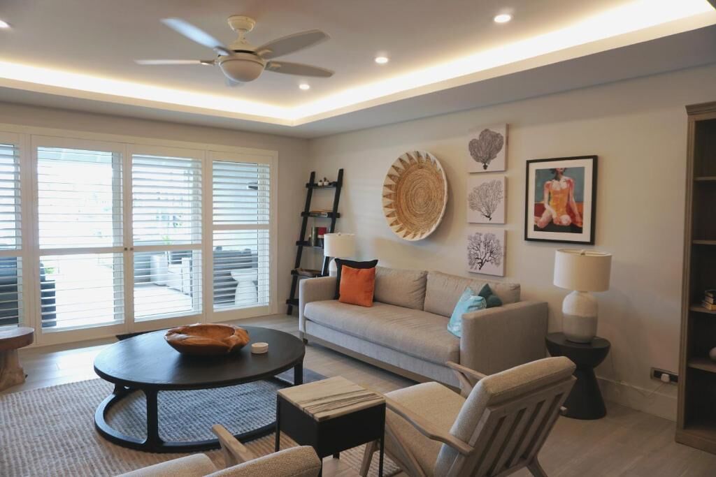 A living room with a sofa, coffee table, and chairs, a ceiling fan, and artwork on the walls.