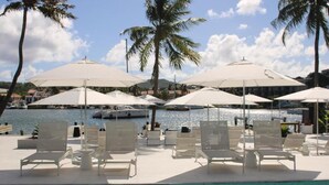 A poolside area with lounge chairs and umbrellas, a clear view of the water, and palm trees.
