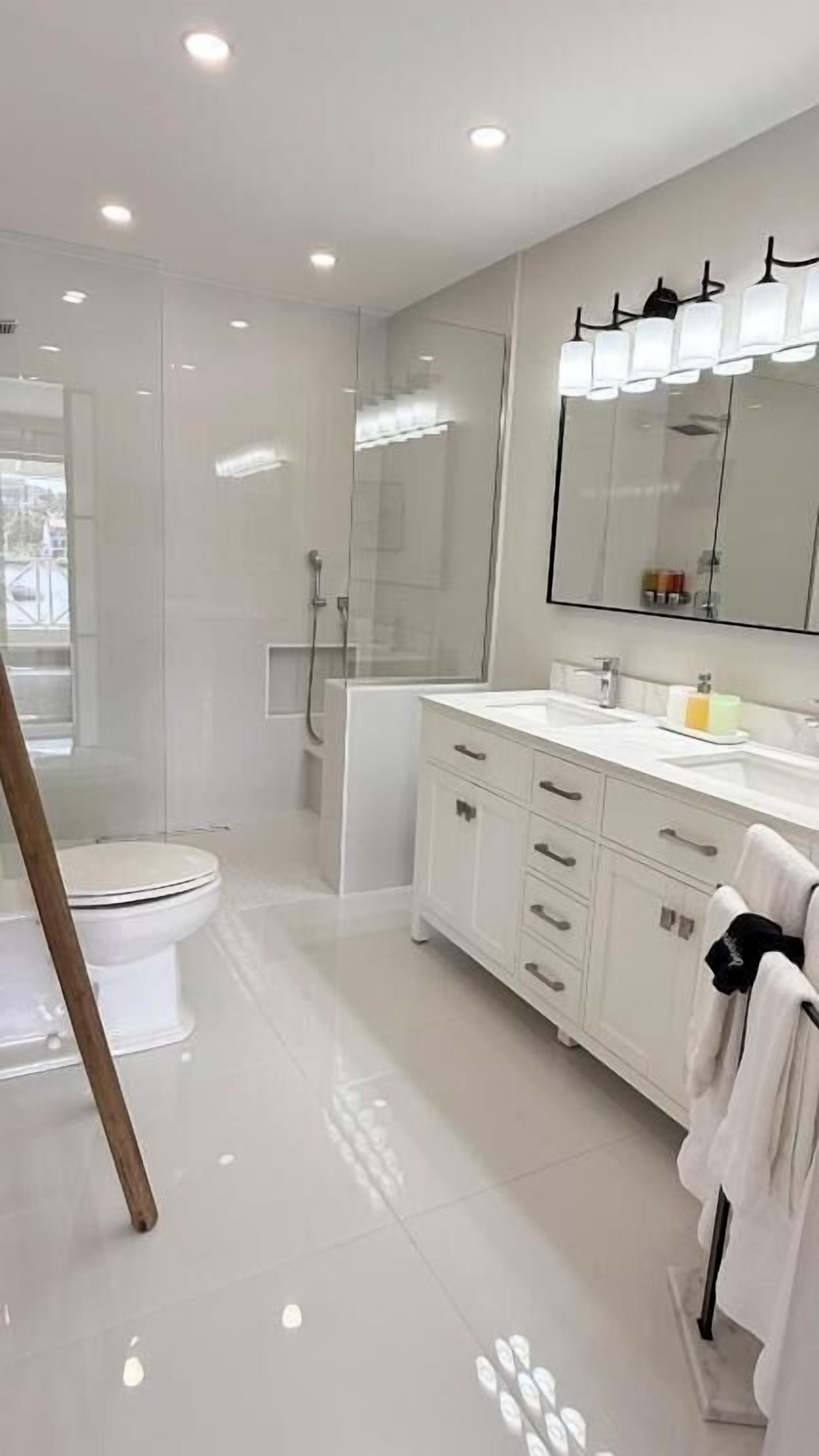 Een moderne badkamer met toilet, douche, wastafel en een grote spiegel.