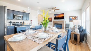 A modern kitchen with a dining area, a fireplace, and a living room with a sofa and TV. - Modern 3BD Home Near TOWN! Hot Tub + Games + VIEWS (Sevierville)