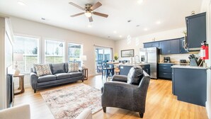 A spacious living area with a sofa, armchair, and rug, a kitchen with dark cabinets, and a ceiling fan. - Modern 3BD Home Near TOWN! Hot Tub + Games + VIEWS (Sevierville)